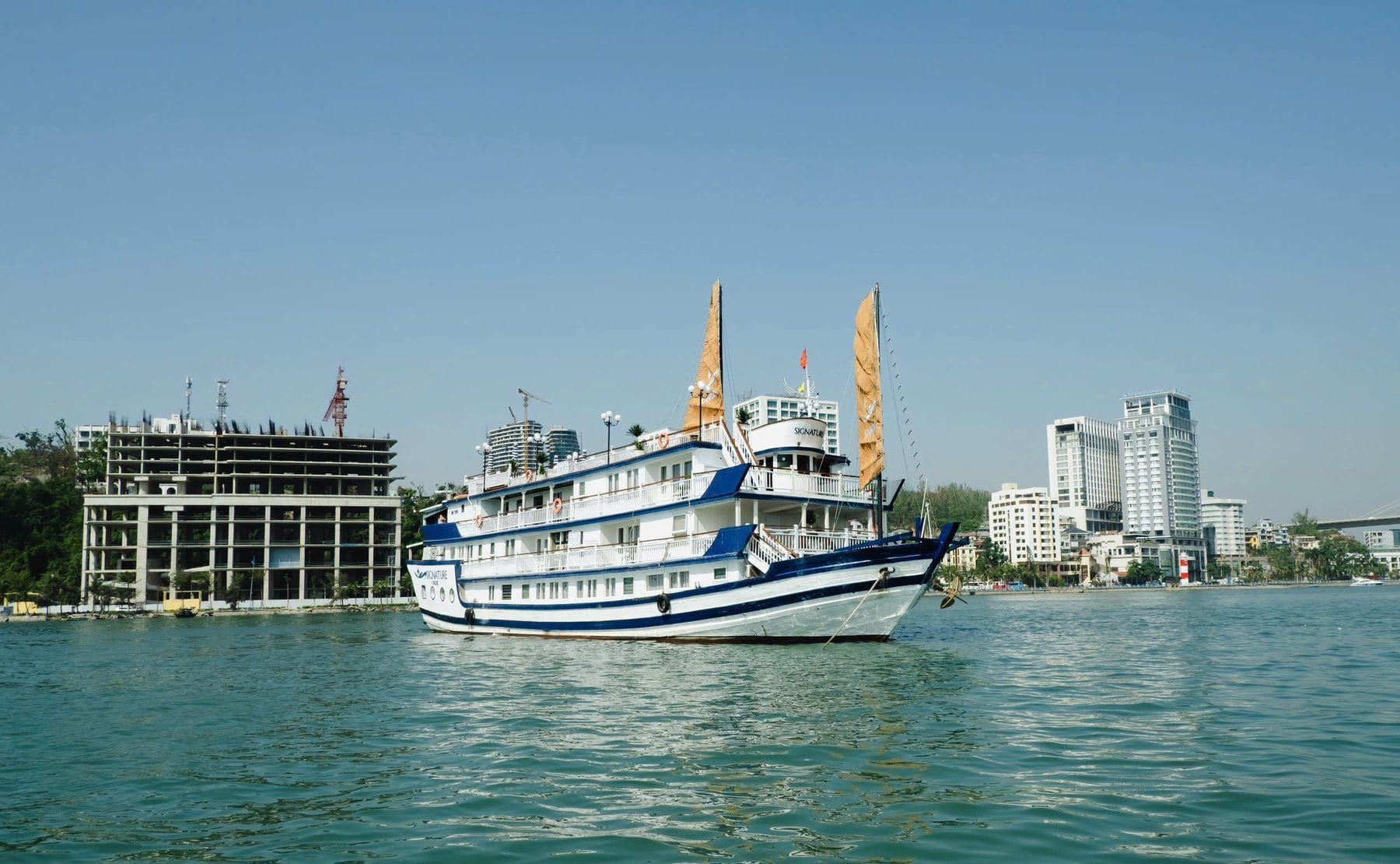 Signature Halong Cruise on the water, dark sails raised above a white hull